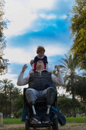 Téléchargez les photos : Amputé âgé et utilisateur de fauteuil roulant profite d'un après-midi avec sa famille, en particulier en jouant avec son fils. - en image libre de droit