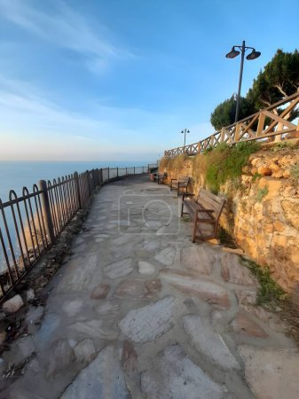 In the peaceful light of the sunset, a quiet and tranquil walking area decorated with stone paths and wooden benches overlooking the sea