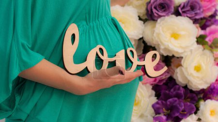 Mujer embarazada en vestido verde con la palabra amor en su vientre