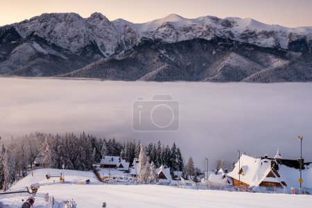 Beautiful sunny winter morning with mountains in the background and fog in the valley. View of the Tatra Mountains with Giewont in Zakopane Town and Koscielisko Village in Poland country.