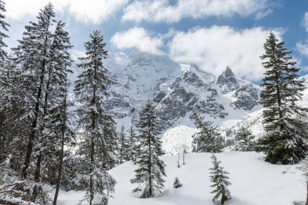 Beautiful Polish Tatra mountains in winter with snowy trees and frozen Mnich (Monk) rocky mountain in background without people with blue sky and clouds in the sunny day