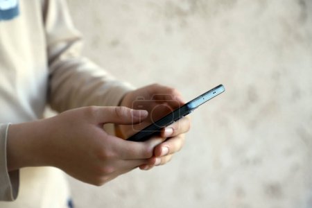 Les mains de l'enfant jouant sur son portable. Adolescent utilisant les réseaux sociaux sur son smartphone. Enfant connecté à la technologie. Fond clair avec espace de copie.