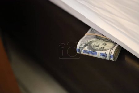Photo for Person keeping money under the mattress. Person hiding their savings in their home. Hand keeping wad of dollar bills on his bed. Concept of distrust in banks and financial entities. - Royalty Free Image