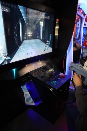 Photo for Arcade game room. Video game park for children and teenagers. Boy playing in Sega Target Bravo video game. Boy shooting a gun in electronic game. Paid electronic games room. Gamer fired video game - Royalty Free Image