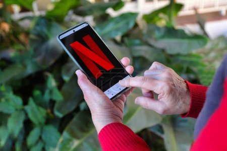 Téléchargez les photos : Mains de personne âgée regardant Netflix sur un téléphone intelligent. Vieille femme utilisant la technologie de streaming. Dame regarder des films en ligne. - en image libre de droit