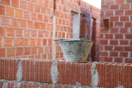 Mason bucket to mix cement in a building under construction with ceramic bricks. Concept of bricklayer work, masonry, construction, architecture, building industry, real estate ventures.