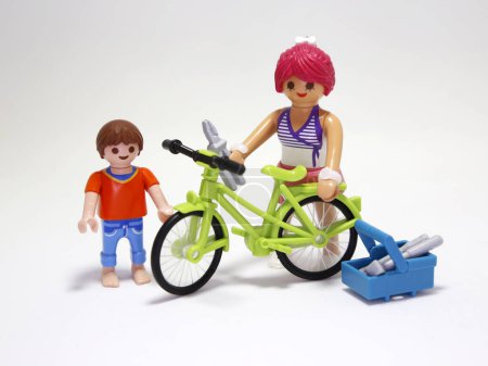 Photo for Playmobil dolls. Young woman fixing a bicycle with a little boy. Friends. Fun and happiness. Toys for children. Isolated white. - Royalty Free Image