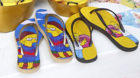 Photo for Flip flops with the characters of The Simpsons. Homer and Lisa Simpson. Summer footwear for the beach and pool. Fun designs. TV characters. Products for sale in a store. - Royalty Free Image