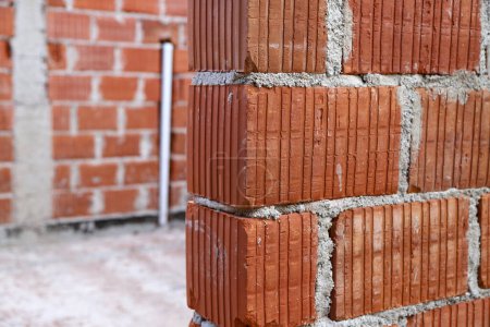 Building under construction with exposed beams and structures. Concept of bricklayer work, masonry, house construction, architecture, building. Building under construction with red ceramic bricks.