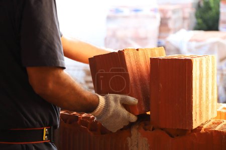 Photo for Mason. Construction worker lifting a brick. Builder working on construction site. Professional bricklayer working on house construction. Concept of architecture, construction, industry. - Royalty Free Image