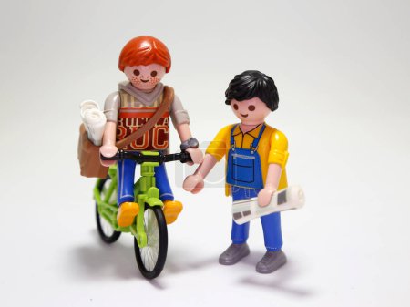 Photo for Newsboy. Playmobil doll. New's paper seller. Newspaper delivery man on a bicycle. Client. Young boy. Paperboy. Newspaper. Redhead with freckles. Boy. Employee. Happy person. Isolated white. Toy. - Royalty Free Image
