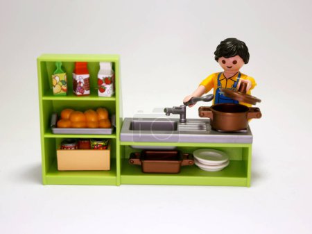 Foto de Playmobil dolls. Man cooking. Man making dinner in their kitchen. Food preparation. Toys for children. Isolated white. Plastic figures. - Imagen libre de derechos