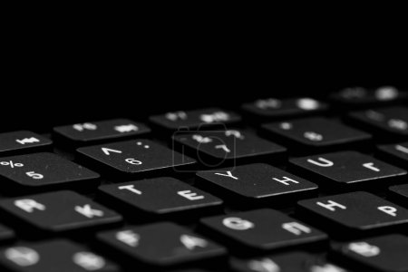 Nahaufnahme schwarzer Tasten mit Wassertropfen. Schwarze PC-Tastatur auf schwarzem Hintergrund. Englische und kyrillische Buchstaben auf der Tastatur.