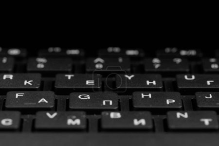 Vue rapprochée des touches noires avec des gouttes d'eau. Clavier PC noir sur fond noir. Alphabet anglais et cyrillique sur le clavier.