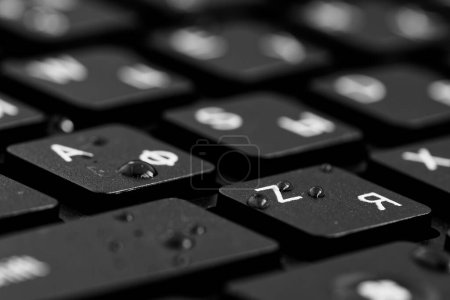 Nahaufnahme schwarzer Tasten mit Wassertropfen. Schwarze PC-Tastatur auf schwarzem Hintergrund. Englische und kyrillische Buchstaben auf der Tastatur.