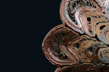 Figura abstracta con la textura de un modelo impreso en 3D, color cobre pintado con manchas de oxidación. Capas de plástico visible, fondo negro, con espacio de copia. 