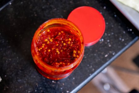 Traditional sauce adjika with hot chili pepper, paste harissa in glass jar on brown table