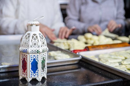 Photo for Mother and daughter are working together preparing pastries for iftar in ramadan with lantern in front, ramadan pattern - Royalty Free Image