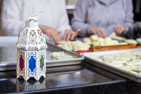 Photo for Mother and daughter are working together preparing pastries for iftar in ramadan with lantern in front, ramadan pattern - Royalty Free Image