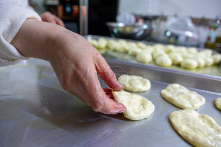 Frau knetet Teig mit den Händen in der Küche auf Metallblech und drückt ihn flach, während sie Olivenöl verwendet