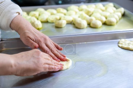 Woman kneads dough with hands in the kitchen on metal tray, pushing it to be flat while using olive oil