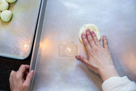 Weibliche Hände flachen Teigbällchen ab und formen sie im Kreis, um sie später zu füllen, Teig von Hand gemacht