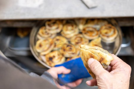 Old man hands holding aluminum plate full of white cheese stuffed pastries and putting it in old oven
