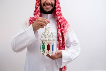 Draped in the dignified attire of Kandoura and Keffiyeh, an Arabic man extends a symbol of hospitality and generosity by holding Fanous. Against a backdrop of purity, to illuminate the essence of Eid