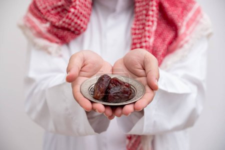arabe homme tenant dates représente l'hospitalité et la générosité portant kandura avec keffiyeh sur fond blanc isolé pour les célébrations de l'Aïd