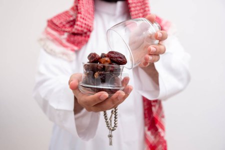 arabic man holding dates represents hospitality and generosity wearing kandura with keffiyeh on isolated white background for eid celebrations