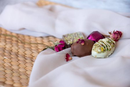 Schokoladenstücke mit eleganten Blumen und Rosen auf rosa und weißem Hintergrund. Romantisches Konzept mit Mock-Up Space zur Anpassung. Ideen für Valentinstag, Feste und Gourmet-Geschenkkonzepte