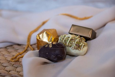 Collar de oro y piezas de chocolate sobre fondo blanco con elegante espacio falso. Concepto de lujo para joyas y chocolates. Perfecto para celebraciones, regalos y eventos. con espacio de copia