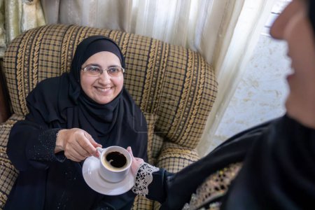 Arabic woman wearing hijab show hospitality for older woman serving her with arabic coffee