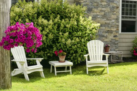 Resting place in the garden near the house. Traditional wooden armchairs and flowers. Selective focus on flowerpot with petunia flowers.