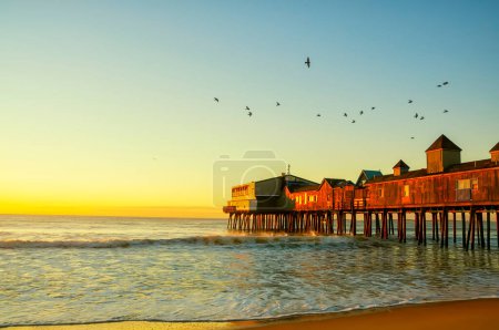 Photo for Old wooden pier on the ocean and birds in the sky in the early morning at dawn. Old Orchard Beach. USA. Maine. - Royalty Free Image
