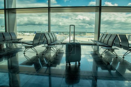 Foto de Una maleta en el edificio terminal junto a la ventana con vistas a los aviones. Filas vacías de asientos en un salón del aeropuerto - Imagen libre de derechos