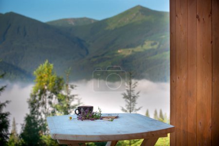 a cup of tea and a notepad for notes on a table with a pitchfork on a mountain summer landscape. Outdoor recreation.