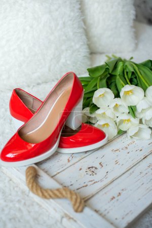 scarlet heeled shoes and white tulip flowers, on a white vintage wooden background.