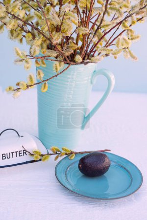 Aguacate, plato de mantequilla y un ramo de sauces juntos en la mesa. humor de primavera, mirada brillante.