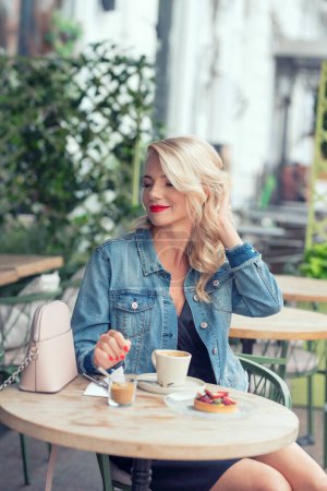 Une jolie femme séduisante, 48 ans, boit un café à une table dans un café de rue.