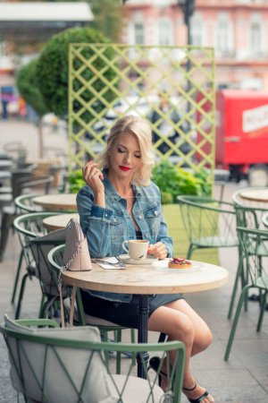 Une jolie femme séduisante, 48 ans, boit un café à une table dans un café de rue.