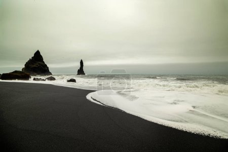 herrlicher Strand mit schwarzem vulkanischen Sand und Felsen. Trollfinger. Island. Schwarz-weiße Farben dramatisches Wetter