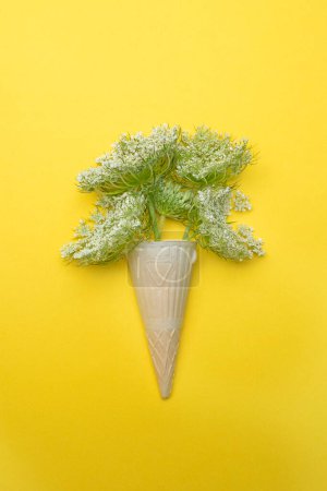 white wildflowers in an ice cream cone on a yellow background. flat top view