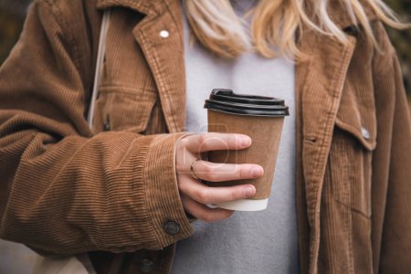 Foto de Una joven sostiene un vaso de café desechable artesanal en su mano en un paseo por el parque, de cerca. - Imagen libre de derechos
