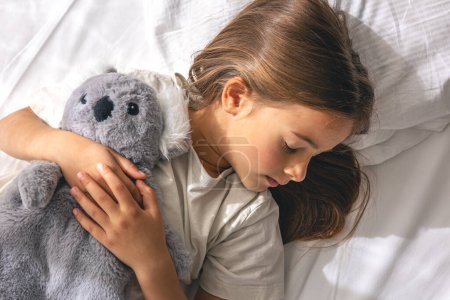 A cute little girl with her favorite soft toy is sleeping sweetly on the bed.