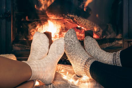 Photo for Womens feet in warm socks are heated by the home fireplace with a bright flame. - Royalty Free Image