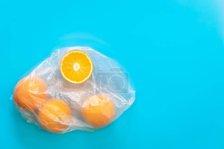 Téléchargez les photos : Oranges fraîches dans un sac en plastique transparent sur fond bleu, pose plate, espace de copie. - en image libre de droit