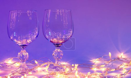Photo for Two empty wine glasses and a garland in neon lighting, Valentines day background. - Royalty Free Image