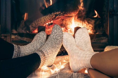 Photo for Womens feet in warm socks are heated by the home fireplace with a bright flame. - Royalty Free Image