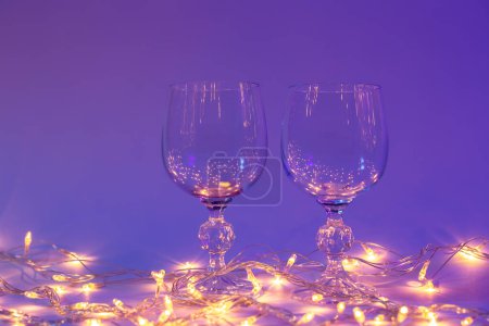 Photo for Two empty wine glasses and a garland in neon lighting, Valentines day background. - Royalty Free Image